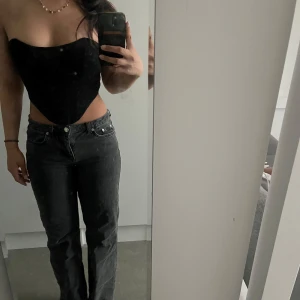 Svart korsettopp med sweetheart-ringning - Säljer en svart korsettopp med snygg sweetheart-ringning och spetsig nederkant. Toppen är axelbandslös och sitter tight runt kroppen för en riktigt smickrande siluett. Perfekt att styla med jeans eller kjol för en cool look.