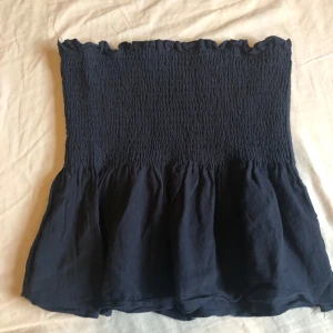 Mörkblå bandeau tubtopp från SHEIN - Supersöt mörkblå bandeau tubtopp från SHEIN i storlek XS. Toppen har smockad överdel och volangig nederkant som ger en cool och feminin look. Perfekt för varma dagar och enkel att matcha med jeans eller kjol.