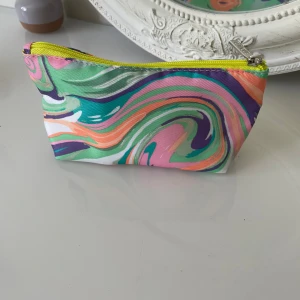 Färgglad necessär från Clinique - En liten och smidig necessär från Clinique med swirlmönster i grönt, rosa, lila, orange och vitt. Väskan har en gul dragkedja och insida i neon-gult tyg. Perfekt för smink eller småprylar i väskan.