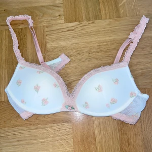 Intimissimi bh med blommor gioia 75B - Romantisk bh i vitt med små rosa blommor och ljusrosa spets längs kanterna och axelbanden. Kuporna är lätt vadderade och sidorna har mesh-tyg. Perfekt för dig som gillar gulliga och feminina underkläder. Storlek 75B från intimissimi, säljs inte längre och är i superfint skick och knappt använd pga för liten