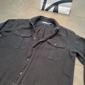 Ralph Lauren overshirt - Tjenare, säljer en svart bomulls overshirt från Ralph Lauren, skicket är väldigt bra skulle säga 9/10. Storleken är S, killen på bilden är 182 cm, släng iväg ett dm för frågor! 