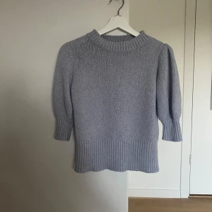 Ljusgrå stickad tröja från NA-KD - Supermysig ljusgrå stickad tröja från NA-KD med bred ribbad kant nedtill och vid halsen. Tröjan har trekvartsärmar med lätt puff och är perfekt för lager-på-lager. Enkel att styla till jeans eller kjol för en chill look.