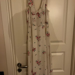 Vit blommig långklänning från BikBok - Supersöt långklänning från BikBok i vitt med rosa och gröna blommor. Klänningen är ärmlös med v-ringning och har en flowy passform som ger en romantisk vibe. Perfekt för sommarens alla tillfällen!
