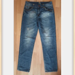 Blå jeans från Northone med slitningar - Snygga blå jeans från Northone med slitna detaljer och kontrastsömmar i gult. Klassisk femficksmodell med raka ben och knappar i brunt och rött. Perfekta för en avslappnad streetstil.