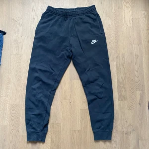 Svarta Nike mjukisbyxor - Svarta mjukisbyxor från Nike med klassisk logga på vänster ben. Byxorna har resår i midjan och vid bensluten, samt sidofickor. Perfekta för chill eller träning, riktigt sköna och stilrena.