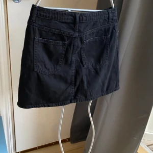 Svart jeanskjol med fickor!  - En svart kort jeanskjol med klassisk femficksdesign, bälteshällor och knapp framtill. Snygg och enkel modell som passar till många olika stilar. Perfekt att matcha med en t-shirt eller hoodie.5 fickor  Endast använd vid ett tillfälle!  100 % bomull  Längd från linning och nedtill 36 cm 