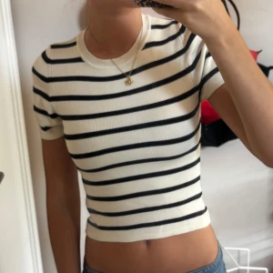 Randig croppad topp från Gina Tricot - Superfin croppad topp från Gina Tricot i vitt med svarta horisontella ränder. T-shirten har korta ärmar, rund halsringning och är ribbad i materialet. Perfekt för dig som gillar en enkel men snygg stil.