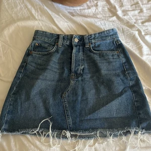 Mörkblå Jeanskjol - Säljer en blå jeanskjol. Kjolen är kort med fransig nederkant. Kjolen är mid waist. 