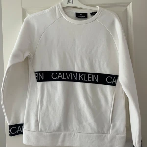 Vit Calvin Klein tröja - Vit sweatshirt från Calvin Klein Performance med svart logoband över bröstet och vid nederkanten. Tröjan har rund halsringning, långa ärmar. Nästan aldrig använd.