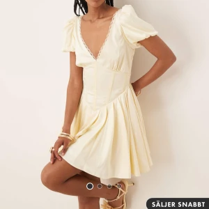 Oanvänd ljus kort klänning - Helt oanvänd och fortfarande kvar i plasten. Superfin ljus kort klänning med puffärmar och djup v-ringning både fram och bak. Klänningen har markerad midja, voluminös kjol och spetsdetaljer längs urringningen. Nypris: 1139kr