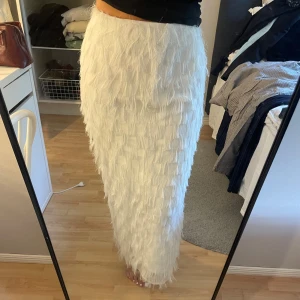 Vit långkjol med fransar  - Vit långkjol från Gina Tricot med fransiga detaljer över hela kjolen. Kjolen har rak passform med en liten slits på sidan nedtill och en dragkedja på sidan upptill. Endast använd 2-3 gånger så den är som ny🫶🏼🤍