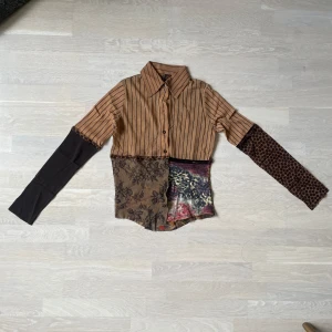 Patchwork skjorta Jean Paul Gaultier - Unik patchwork mesh skjorta från Jean Paul Gaultier Soleil med bruna och svarta ränder, blommigt spetsmönster och leoparddetaljer. Skjortan har lång ärm, knappar framtill och mixade material som ger en cool, edgy vibe. Perfekt för dig som vill sticka ut med din stil.