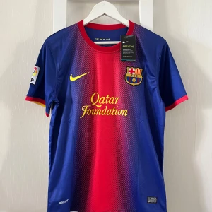 FC Barcelona Messi 10 matchtröja Nike M - Barça-fans, här är en officiell FC Barcelona matchtröja med Messi 10 på ryggen. Tröjan är blå och röd med gula detaljer, tillverkad i lätt och ventilerande polyester. Klassisk Nike Swoosh, Qatar Foundation-tryck och LFP-märke på ärmen. Perfekt för dig som älskar fotboll och Messi.