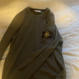 Mörkgrå stickad tröja från Stone Island - Säljer en mörkgrå stickad tröja från Stone Island med den klassiska loggan på vänster ärm. Tröjan har rund halsringning och långa ärmar, perfekt för lager-på-lager under kyliga dagar. Enkel och stilren design som passar till det mesta. Fungerande qr kod. Kom med bud!!