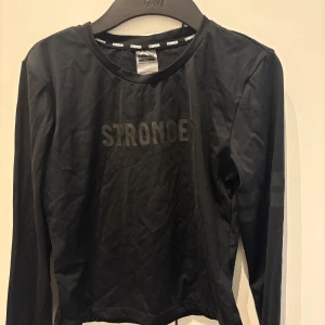 Svart långärmad träningströja - Svart långärmad träningströja från Stronger med diskret logga framtill. Tröjan är tillverkad i ett stretchigt material med hål på i ryggen. Aldrig använd!💕