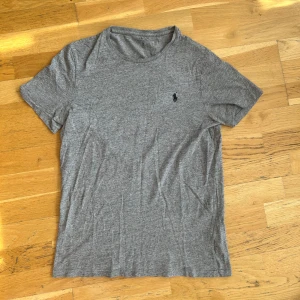 Grå t-shirt från Polo Ralph Lauren - Säljer en klassisk grå t-shirt från Polo Ralph Lauren med en broderad logga på bröstet. T-shirten är kortärmad och tillverkad i mjuk bomull