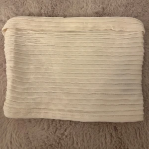 Vit bandeau tubtopp  - Säljer en vit bandeau tubtopp från SHEIN i storlek XS. Toppen har ett ribbat, vågigt mönster och är ärmlös. Perfekt att styla med jeans eller kjol för en fräsch look. Materialet känns mjukt och stretchigt.