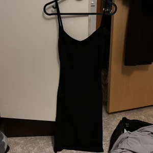 Svart ribbad kort klänning  NA-KD - Svart kort klänning  från NA-KD med smala axelband och v-ringning. Klänningen är ribbad och har en tight passform som framhäver . Materialet känns mjukt och följsamt.