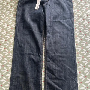 Mörkblå jeans från DNY med bälte - Mörkblå raka jeans från DNY i bomull och elastan, med snygga kontrastsömmar och ett coolt brunt bälte med nitar och mässingsspänne. Klassisk femficksmodell och normal passform. Perfekta för dig som gillar en tidlös jeanslook.