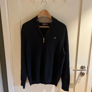 Marinblå merinoulltröja Morris half zip  - Snygg marinblå långärmad tröja från Morris i 100% merinoull. Klassisk modell med half zip och liten broderad logga på bröstet. Perfekt för dig som gillar stilrena och bekväma plagg med premiumkänsla. Storleken är XL i barnstorlek men sitter som S. Modellen på bilden är 182 cm lång. Nypris på tröjan är 1800kr