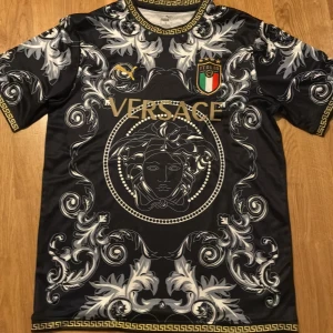 Italien puma fotbollströja - Unik svart fotbollströja från Puma, med stora barockinspirerade mönster i vitt och grått, gulddetaljer och Italiens landslagsemblem. Kortärmad modell i lätt polyester.