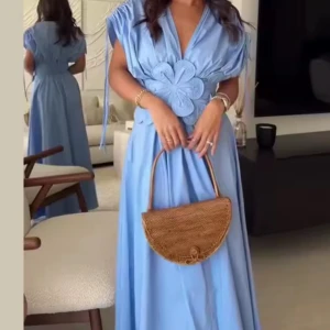 Ljusblå långklänning med blomdetalj - Superfin ljusblå långklänning med djup v-ringning och stor blomapplikation i midjan. Klänningen har korta ärmar med knytband och ett flowy fall som ger en riktigt drömmig vibe. Perfekt för dig som vill sticka ut med en unik och feminin look.