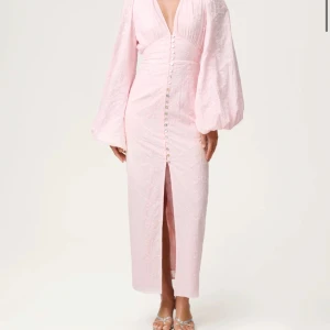 Ljusrosa långklänning med puffärm - Superfin ljusrosa långklänning med v-ringning, puffiga långärmar och knappar framtill. Klänningen har en slits framtill och är dekorerad med subtilt blommönster i tyget. Perfekt för dig som vill sticka ut med en romantisk look. Helt nytt skick, har inte ens testat den, då jag beställde 2 storlekar🌸💓