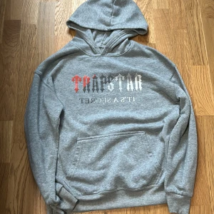 Grå tracksuit från Trapstar - Snygga grå tracksuit från Trapstar med elastisk midja och logga tryckt på ena benet. Byxorna är i mjukt bomullsmaterial och har en avslappnad passform, perfekta för chill dagar eller streetwear-stil.