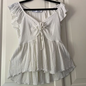 Vit volangblus fråg Lager 157 - Supersöt vit volangblus från Lager 157 med volangärmar och liten knytning fram. Den har rynkad struktur och är lätt v-ringad. Jättefin till ett par jeans eller kjol💕Knappt använd.