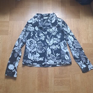 Svartvit blommig skjorta  - Svart skjorta från Cappuccini i storlek L med stora vita blommor. Skjortan har långa ärmar och knäppning framtill. Två bröstfickor som är dolda. ❤️😊 kan nog vara en overshirt också. Pris är diskuterbart vid snabb affär 🩷