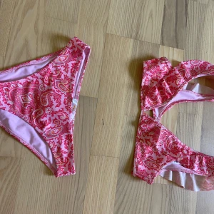 Rosa bikini med paisleymönster Gina Tricot - Snygg bikini från Gina Tricot i rosa med paisleyinspirerat mönster i olika rosa och röda nyanser. Bikinin har klassisk form med breda axelband och mjuk resår. Perfekt för strandhäng och pooldagar.
