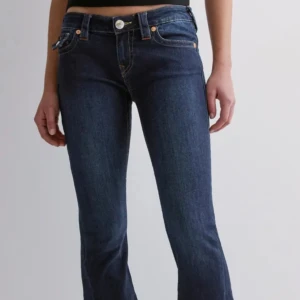 True Religion mörkblå bootcut jeans - Säljer ett par ikoniska mörkblå jeans från True Religion med låg midja och bootcut. Jeansen har snygga kontrastsömmar, klassiska fickor med lock och silverfärgade knappar. Perfekt för dig som vill ha en tidlös och trendig look. Som nya, prislappen är kvar, nypris 1300 men pris kan diskuteras💕
