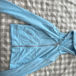 Ljusblå hoodie med dragkedja - Säljer en ljusblå hoodie med dragkedja och fickor framtill. Perfekt för en avslappnad stil. Den har långa ärmar och en bekväm huva.