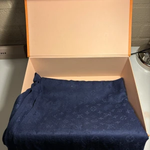 Halsduk - Elegant mörkblå halsduk  med ett subtilt mönster av märkets ikoniska logotyper. Halsduken har fransar längs kanterna och ger en lyxig känsla. Perfekt för att lyfta vilken outfit som helst. Kommer i originalförpackning.