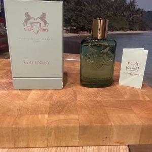 Greenley parfym från Parfums de Marly - Greenley från Parfums de Marly är en elegant parfym i en stilren grön flaska med en lyxig guldfärgad kork. Förpackningen är ljus med märkets logotyp i silver. Perfekt för den som söker en fräsch och sofistikerad doft.
