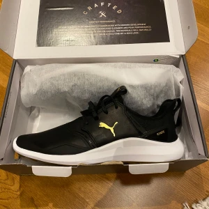 Svarta Puma Ignite NXT Crafted skor - Säljer ett par svarta Puma Ignite NXT Crafted skor med guldiga detaljer. Skorna har en vit sula och är vattentäta, vilket gör dem perfekta för olika väderförhållanden. De har en stilren design med snörning och en bekväm passform.