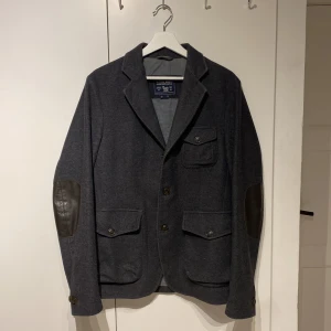 Woolrich vårjacka - Säljer denna väldigt snygga jacka/kortare rock/kavaj från Woolrich! Storleken som står är medium och den passar medium men kanske även en större small. Den är i riktigt bra skick och jag hittade inga defekter! Den är i ull, fodrad med polyester/bomull och armbågslapparna är i äkta läder. Woolrich har också väldigt högkvalitativa plagg så förvänta dig en lång livslängd om du köper. Helt perfekt nu till våren för dig som vill höja din stil. Skriv om du har frågor eller prisförslag! 