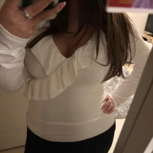 Vit blus med volangdetaljer - Säljer en elegant vit blus med volangdetaljer och v-ringning. Blusen har långa ärmar och en figurnära passform, perfekt för en stilren look. Toppen är från new yorker och har aldrig använts.