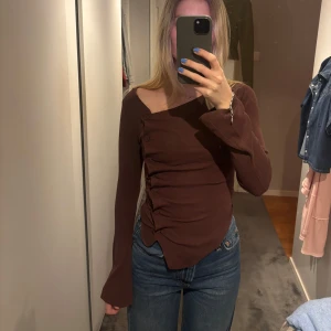Brun långärmad topp från Zara - Säljer en snygg brun långärmad topp från Zara med asymmetrisk design och knappar längs sidan. Skulle säga att den är lite mörkare och kallare ton i verkligheten🤎🤎🤎🤎