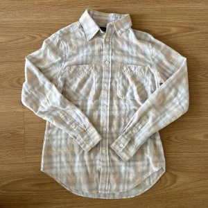 Beige rutig skjorta från Ralph Lauren - Snygg beige rutig skjorta från Ralph Lauren med klassisk krage och knappar framtill. Skjortan har två bröstfickor och långa ärmar med knappar vid ärmsluten. Jag säljer den på grund av att den var för liten. 160 S.