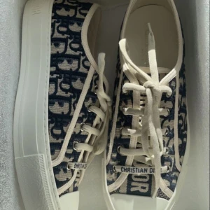 Sneakers från Christian Dior - Snygga sneakers från Christian Dior med ett unikt mönster i blått och beige. Skorna har snörning och en vit sula som ger en stilren look. Perfekta för att lyfta din outfit med en touch av lyx. [Pris kan diskuteras] [Kvitto finns]