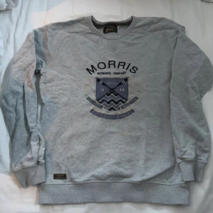 Grå sweatshirt från Morris - Säljer en stilren grå sweatshirt från Morris med ett tryck på framsidan. Tröjan har långa ärmar och ribbade muddar vid ärmslut och nederkant. Perfekt för en avslappnad stil.