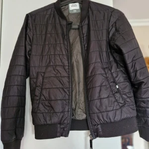 Svart quiltad jacka från McKinley - Säljer en svart quiltad jacka från McKinley. Jackan har en dragkedja framtill och ribbade muddar vid ärmslut och nederkant..