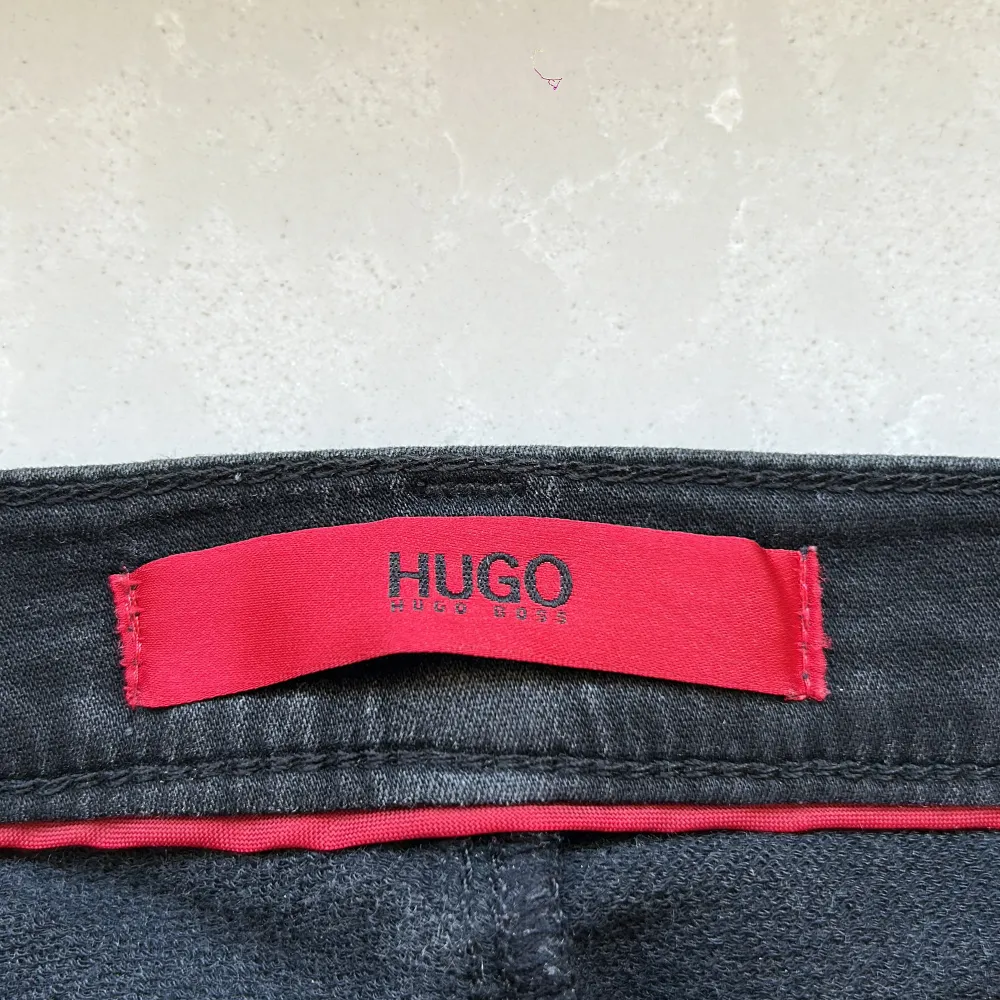 Snygga svarta jeans från Hugo med klassisk femficksdesign och knappgylf. Byxorna har en stilren look med subtila detaljer och en röd insida vid linningen. Perfekta för en stilren och modern outfit. Scick 8/10 priset är ej hugget i sten. Farkut & Housut.