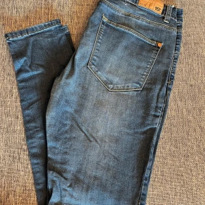 Blå jeansbyxor - Snygga blå jeansbyxor med en tight passform. De har en klassisk femficksdesign och är perfekta för en stilren look. Byxorna är högmidjade och tillverkade i ett stretchigt material för extra komfort.