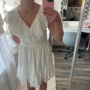 Vit klänning med volangdetaljer - Säljer en söt vit klänning med volanger och v-ringad hals. Perfekt för studenten och  sommarens alla tillfällen. Klänningen är från bubbelroom och är använd en gång💕ny pris 799kr