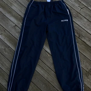 Blåa byxor från Nike - Säljer ett par blåa vintage byxorna från Nike med vita detaljer och logga på sidan. Byxorna har snöre i midjan så passar alla. 