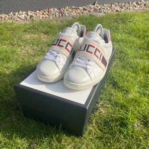  Gucci - Självklart! Här är den uppdaterade annonsen:  Säljer ett par stiliga Gucci sneakers i vit läder med röda och blå ränder. Skorna är i utmärkt skick och kommer med kvitto, dustbag och originalbox. Perfekta för att ge din outfit en lyxig touch! Finns i storlek 40. Priset är 2500kr, men kan gå ner vid snabb affär. Kontakta mig för mer information! Missa inte chansen att äga dessa klassiska sneakers! 🏷️👟