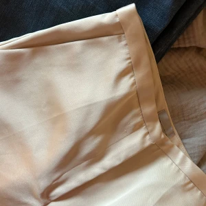Kostymbyxa silke champagne - Snygga champagne färgade byxor från H&M i en stilren design. Byxorna har en rak lös passform och är väldigt bra kvalitet! Älskar dessa byxor och de passar till jättemycket, storlek 36. Fina detaljer vid midjan!