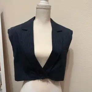 Snygg svart croppad väst med diskreta ränder och v-ringad design. Perfekt för att ge en stilren touch till din outfit.